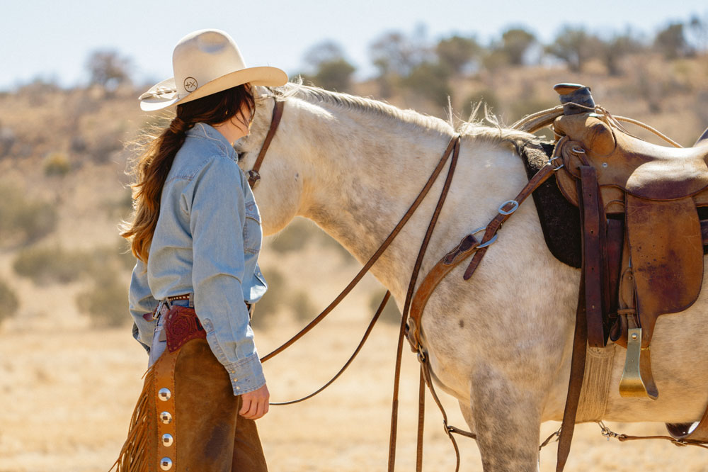 A woman wearing a cowboy hat while standing next to a horse.